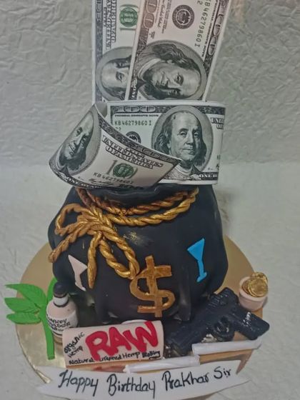 A detailed money bag cake, sculpted to look like a sack of cash with edible dollar bills pouring out. The design also includes other fun elements like a toy gun and RAW rolling papers.