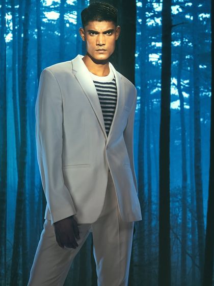 A stark, blue-toned forest is projected behind the model. The lighting is cool and directional, creating a mysterious and high-fashion look that contrasts with the classic suit.