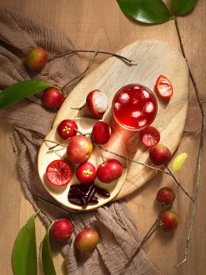 This composition showcases the Kokum fruit in various forms. The overhead lighting creates a clean, bright look while still highlighting the fruit's vibrant red color and unique shape.