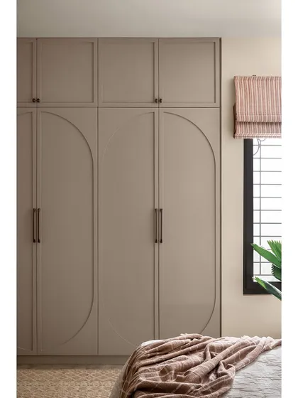 The wardrobe in the guest bedroom features a simple yet elegant design with large, curved grooves on the shutters. The neutral, earthy paint color complements the room's minimalist Wabi-Sabi aesthetic.