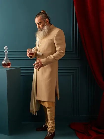 The full look of our beige draped sherwani, paired with a churidar. This outfit is perfect for a daytime wedding or a sophisticated evening event, offering a unique and memorable style.
