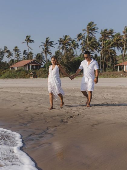 A classic shot of the couple walking along the shoreline in all-white outfits. It's a clean, timeless, and romantic beach portrait.