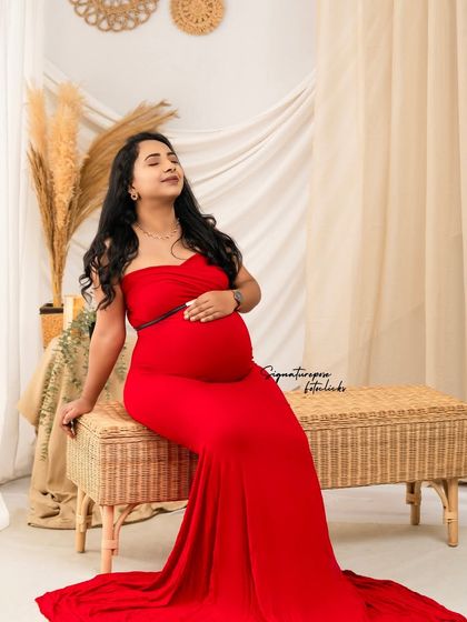 The vibrant red gown provides a stunning pop of color against the neutral tones of the boho wicker bench and backdrop.