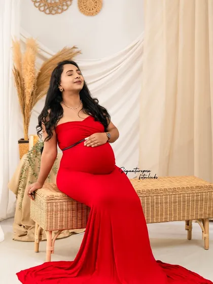 The vibrant red gown provides a stunning pop of color against the neutral tones of the boho wicker bench and backdrop.
