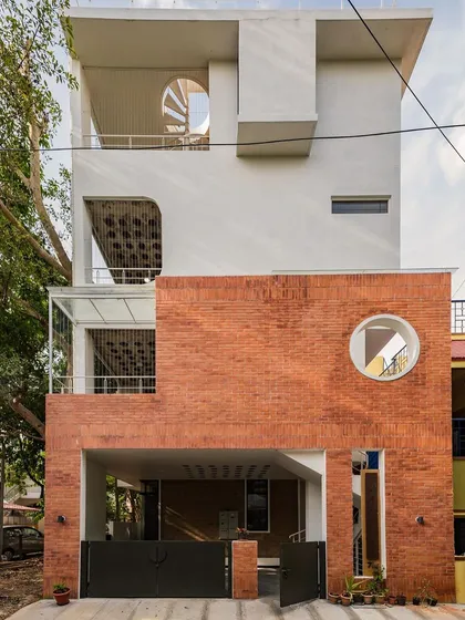 For this urban home in Bangalore, we contrasted a clean white facade with the raw texture of rat-trap bond brickwork. The circular window and spiral staircase are not just design elements; they are invitations to explore the different levels and how light moves through the space.