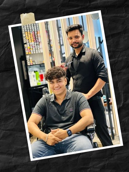 A happy client and his stylist posing after a fresh haircut. The textured curls on top with faded sides is a popular and modern look for men.