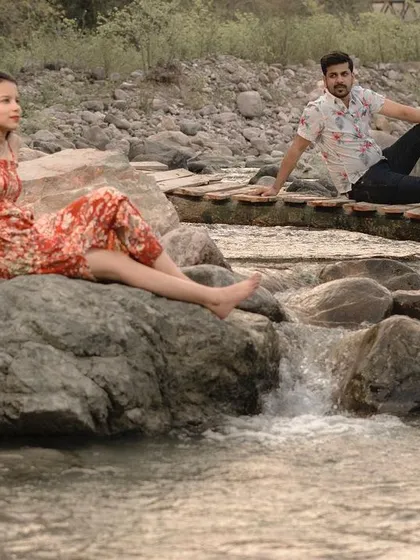 A wide shot of the couple relaxing by a stream in a rocky, natural landscape, perfect for an adventurous pre-wedding session.