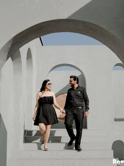 A stylish shot of a couple walking hand-in-hand through a modern, arched hallway. Their all-black outfits and confident stride give this a chic and contemporary pre-wedding feel.