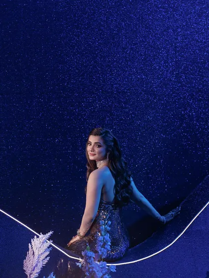 A beautiful portrait moment for the bride, seated against a deep blue, sparkling backdrop that mimics a starry night sky, enhanced by a clean, curved line of light.