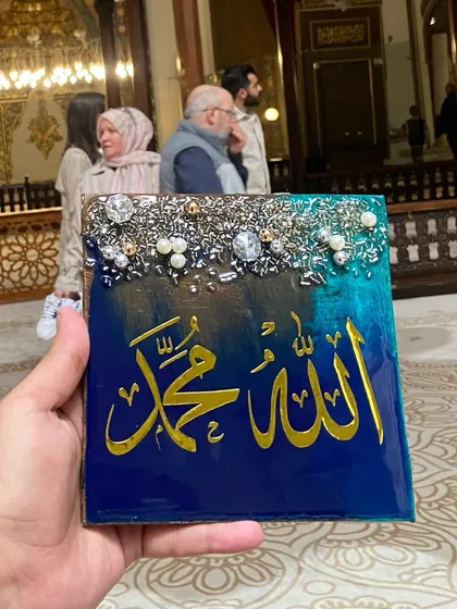 A small, portable frame featuring the names of Allah and Mohammed. This piece, with its blue and green background, was photographed inside the majestic Grand Mosque of Bursa, Turkey.