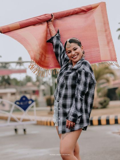 A playful shot of the bride in her shorts and flannel shirt, holding up her wedding saree with a big smile.