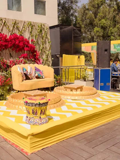The main stage for a vibrant Haldi, featuring a yellow sofa, a bamboo backdrop with bougainvillea, and a custom yellow and white chevron-patterned floor.