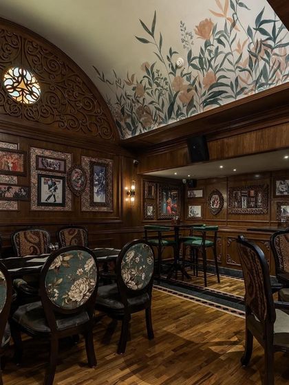 A cozy seating area in the pub, with floral-upholstered chairs and a hand-painted mural on the vaulted ceiling, creates an intimate atmosphere.