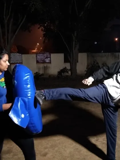 Training doesn't stop when the sun goes down. Here, a student practices powerful kicks on a strike shield during a night session, building strength and dedication.