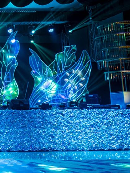 Another angle of the Sangeet stage, showing the relationship between the shimmering facade, the illuminated leaf structures, and the kinetic chandelier.