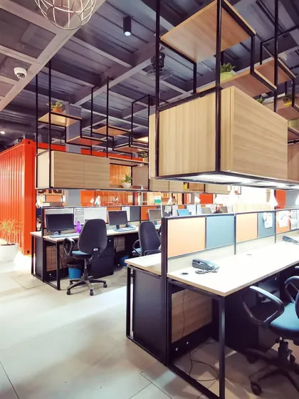 The open-plan workspace at the Tata Hitachi office, featuring suspended shelving and workstations arranged for collaboration. The design uses a mix of industrial materials and natural wood tones to create a productive and inspiring atmosphere.