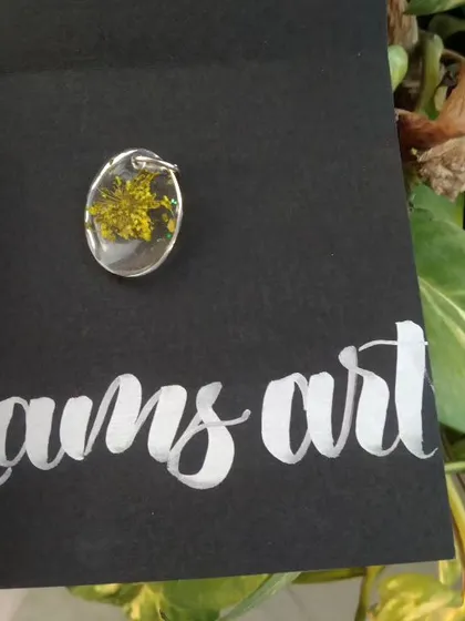 A close up of a small oval pendant with a tiny yellow flower inside, presented on my custom 'Lams art' card.