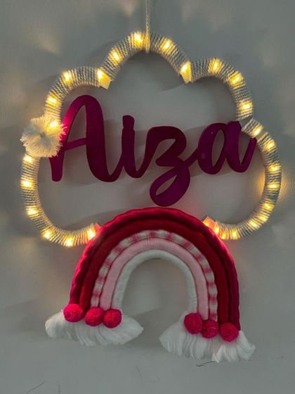 This pink-themed name hanging for Aiza is so vibrant and cheerful. The added pom-poms and fairy lights make it an eye-catching centerpiece for any little girl's room.