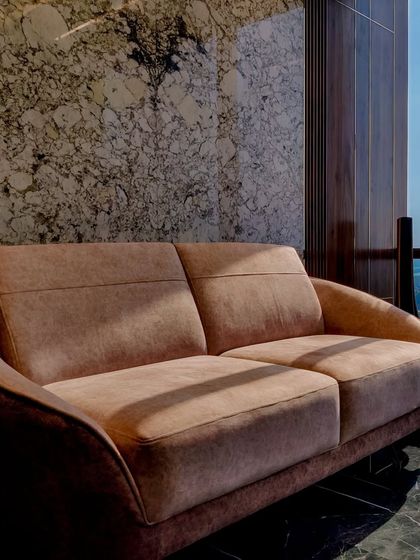 A detail of the plush seating in Mr. Siraj's cabin, set against a dramatic marble wall. The contrast between the soft fabric, the polished stone, and the warm wood creates a sense of understated grandeur.