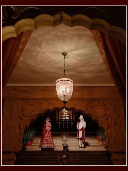 A grand, symmetrical shot of the couple standing on a majestic staircase at Suryagarh. The opulent architecture and dramatic lighting create a powerful and regal wedding portrait.