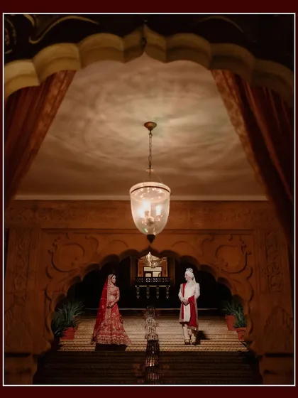 A grand, symmetrical shot of the couple standing on a majestic staircase at Suryagarh. The opulent architecture and dramatic lighting create a powerful and regal wedding portrait.