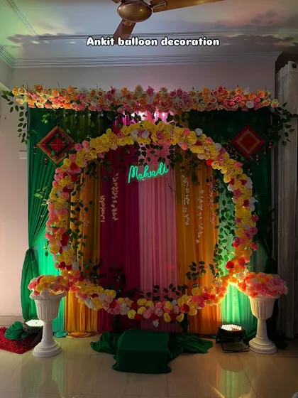 A Mehndi decoration featuring a full ring of yellow and pink flowers against a green and multi-colored drape background.