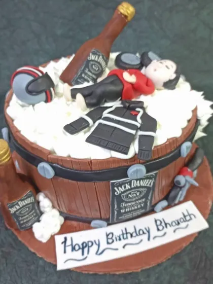 A fun and detailed cake for a Jack Daniel's and bike lover. The design features a barrel, miniature bottles, and a fondant figure passed out on top.