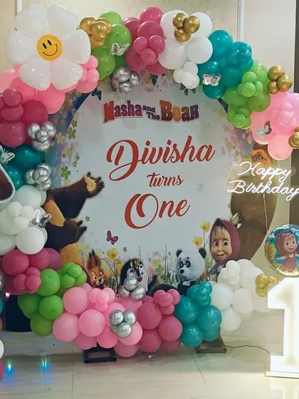 A sweet Masha and the Bear theme for a first birthday. This setup features a circular backdrop with character prints, a colorful balloon garland, and a light-up number '1' for a charming celebration.