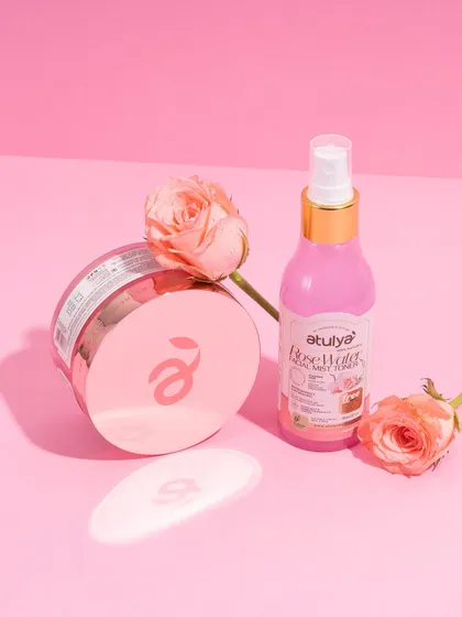 A simple and pretty shot of rose water and face cream with fresh roses against a pink background. The clean lighting and soft shadows create a delicate and feminine aesthetic.