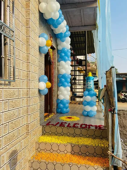 The entrance of a home decorated for a baby boy's arrival, with a blue and white balloon arch and flower-covered steps.