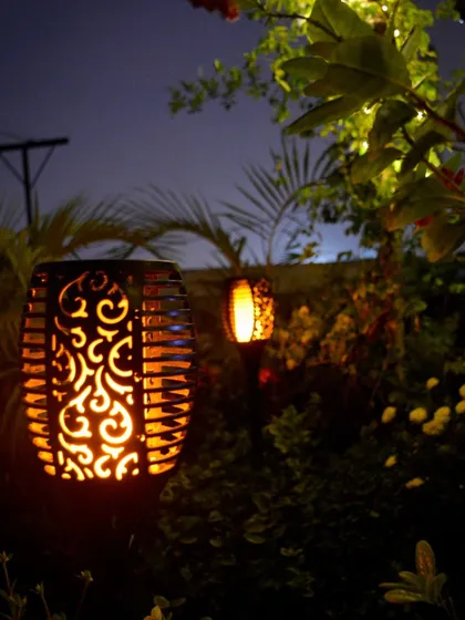 A close-up of one of the solar-powered torch lights. The intricate pattern and flickering flame effect provide a beautiful and sustainable way to light up a garden path.