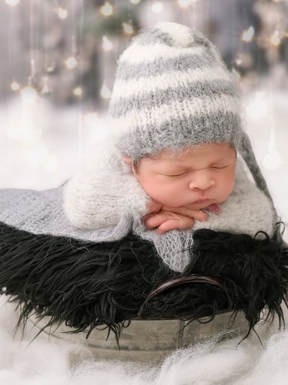 A winter wonderland scene with a baby in a striped hat sleeping in a bucket, surrounded by soft white fluff and a sparkling bokeh background.