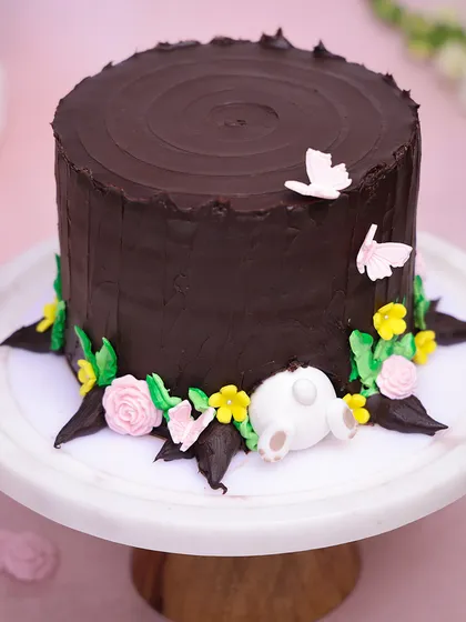 Our Easter Burrow Cake features a rich chocolate frosting that looks like a tree trunk, with a cute bunny burrowing into a floral base.