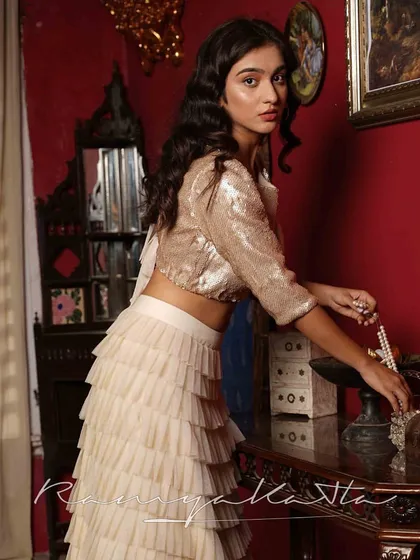 Set in a vintage-inspired room, this beige sequin top and frilled lehenga create a look of old-world glamour, perfect for a themed sangeet or cocktail event.