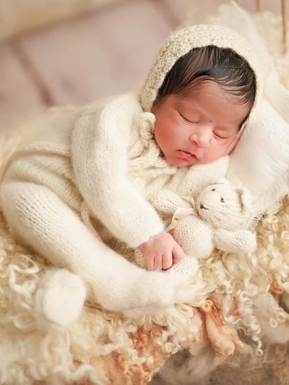 Tiny miracles and big moments. This baby is sleeping soundly on a miniature bed with a tiny teddy, dressed in a cozy white knit outfit.