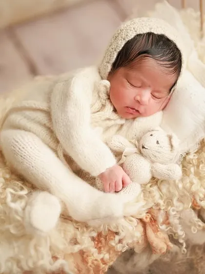 Tiny miracles and big moments. This baby is sleeping soundly on a miniature bed with a tiny teddy, dressed in a cozy white knit outfit.