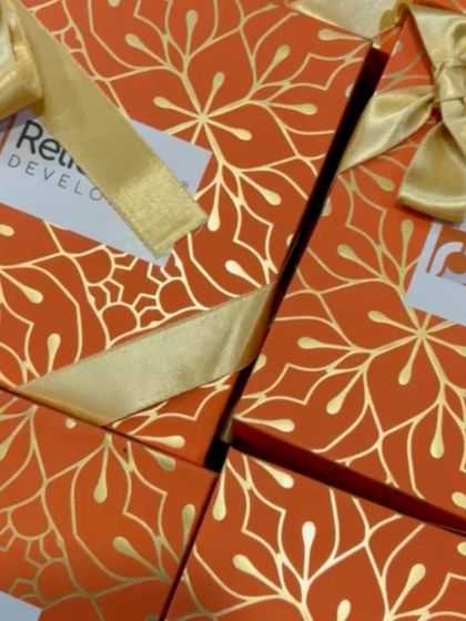 A close-up of the custom-designed box sleeves for the Reliaable Developers Diwali project. The orange and gold foil design adds a touch of festive opulence.
