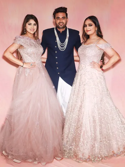 A stylish trio ready for a celebration. The gentleman in the center is wearing a navy blue Indo-western jacket, flanked by two ladies in beautiful rental gowns.
