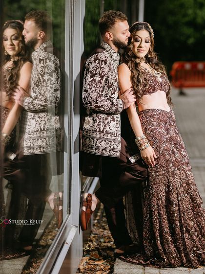 A stylish and moody shot of the couple leaning against a reflective window, creating an artistic and modern wedding portrait.