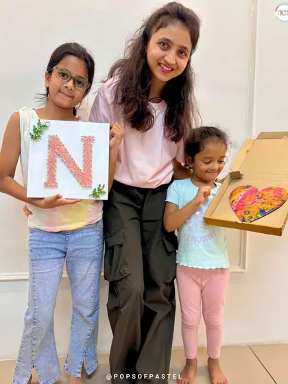 Art brings everyone together. Two young sisters proudly show their string art and fluid art creations alongside their instructor.