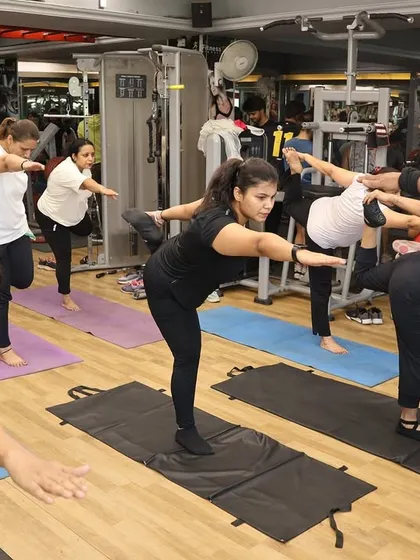It's not all high-intensity. I also guide you through yoga sessions to improve flexibility and find balance. Here, I am helping a member perfect her Virabhadrasana III (Warrior III) pose for better stability.