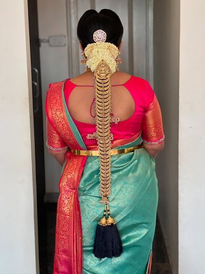 A detailed view of the back of Supritha's bridal look. The hairstyle features a traditional braid adorned with elaborate gold Jadde Billai, perfectly complementing her stunning Kanchipuram silk saree.