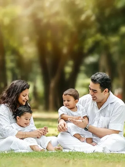 A family with twin boys enjoying a picnic-style setup in a park. The all-white outfits create a classic, clean look against the green grass.