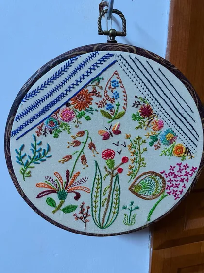 Hoop art allows me to paint with thread, creating detailed botanical scenes that can be treasured forever. This piece combines various freestyle stitches to capture the delicate forms of flowers, leaves, and a butterfly, turning a simple hoop into a captivating piece of wall decor.
