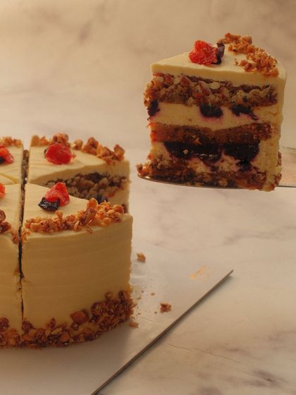 A perfect slice of our Red & Black Dilli Carrot Cake. It features layers of red carrot cake, black carrot halwa, and a whipped cream cheese frosting, topped with candied walnuts.