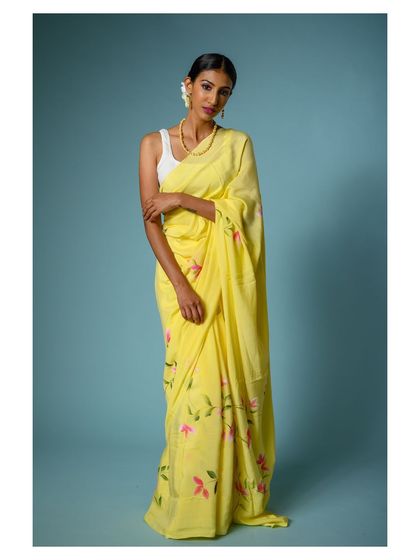 A full-length shot of a vibrant yellow saree with pink floral details. The solid blue background creates a beautiful color contrast, making the image pop.