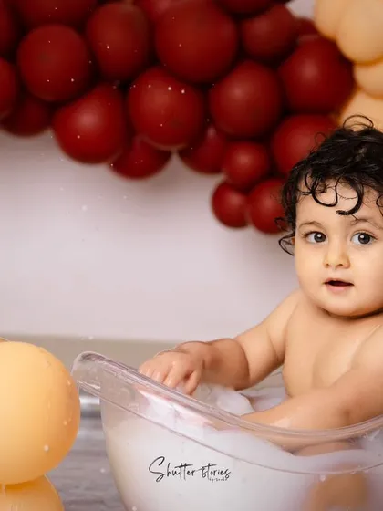 A happy baby boy enjoys a splash in the tub, surrounded by a colorful balloon arch.