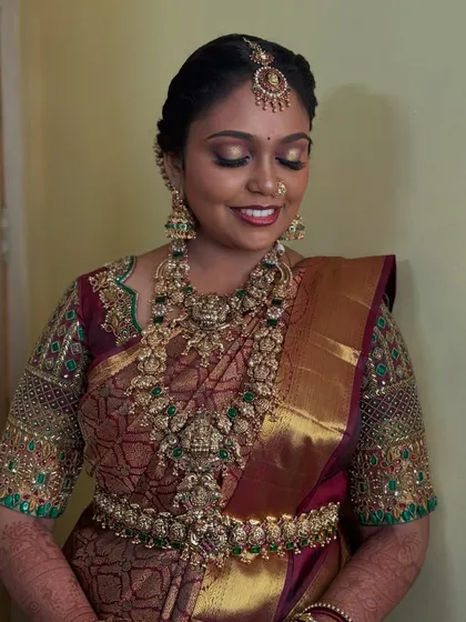 A smiling portrait of Prithivi, showcasing her complete Muhurtham look. The gold and green tones in her jewellery and saree are complemented by a warm, glowing makeup application.