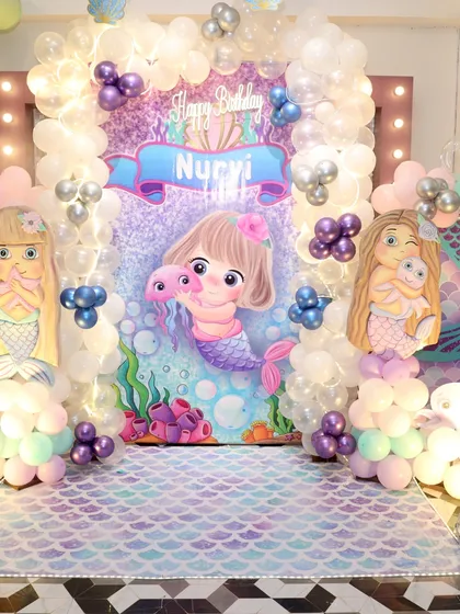 A closer look at the main backdrop for Nurvi's mermaid-themed party. The cute illustrations and soft lighting create a whimsical atmosphere perfect for celebrating.