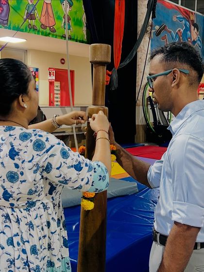 A coach and a parent tie a sacred thread and marigold flowers to the Mallakhamb pole during our Dussehra puja. This ritual symbolizes our respect and gratitude for the sport.